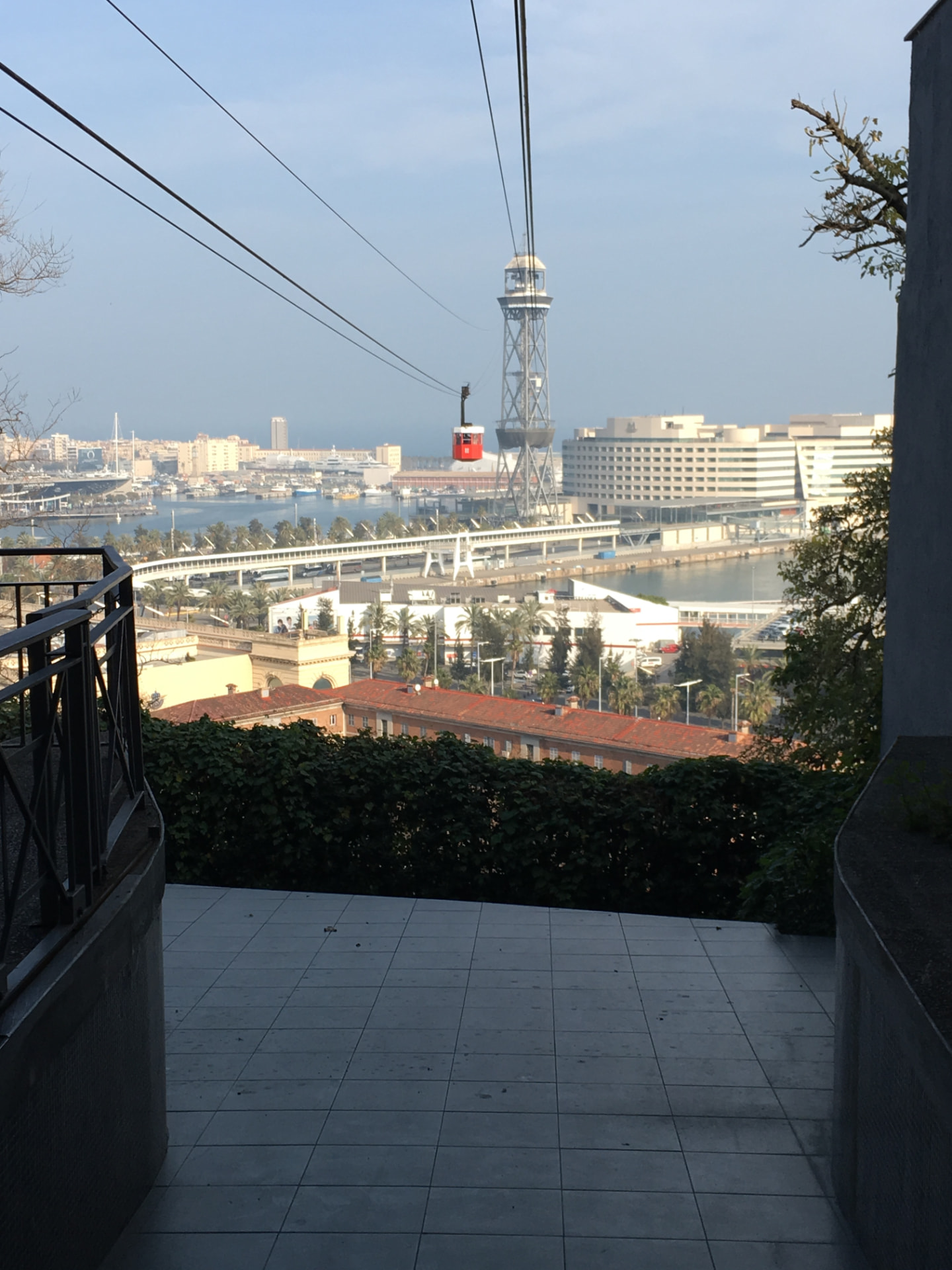 A red cable car cabin crossing above the port of Barcelona, with the harbour tower and waterfront beyond.